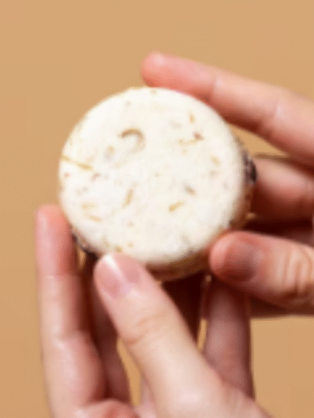 manos sujetando un champu solido de avena redondo